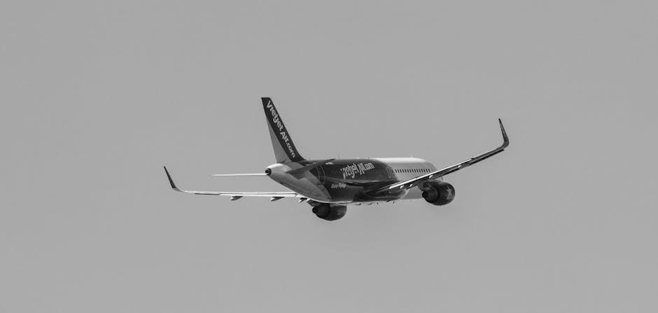 A commercial jet aircraft painted in red and white livery is flying in clear blue sky, with its landing gear extended as it prepares to land or is in descent. The airplane's fuselage features branding